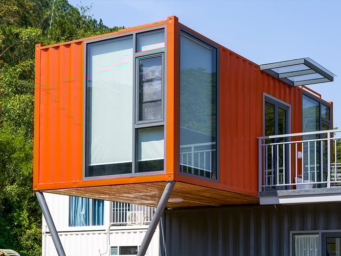 Casa moderna hecha de contenedores marítimos reciclados, con un diseño modular y acabados modernos en color naranja, ubicada en un entorno natural