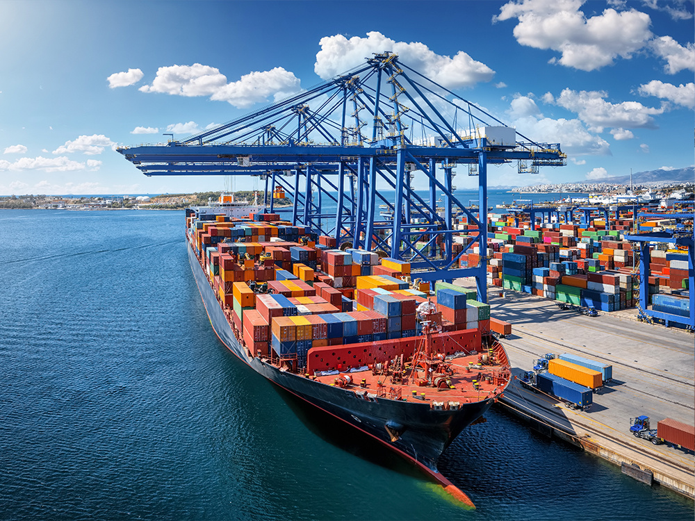 Barco portacontenedores atracado en un puerto internacional, rodeado de grúas y pilas de contenedores listos para su distribución.